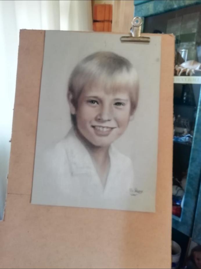 The same portrait of Will clipped to a cardboard board in a room.